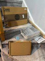 Group of boxed items on stairs including flat frame box, stacked acrylic boxes, long shade box, laptop stand box