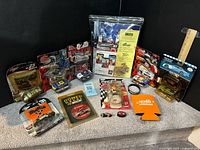 Group shot of all items in lot including die-cast cars, figure, emblem, koozie, wristband, erasers, sealed program package