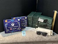 Two sealed Fishmas advent calendars, stacked Novochase sunglasses boxes, unpacked black fashion sunglasses, reading glasses sleeve