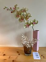 Pink ceramic vase with orchid spray and smoked glass vase on wooden surface