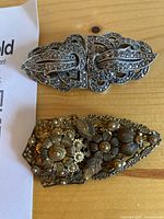 Front view of both sweater clips showing filigree designs and colours