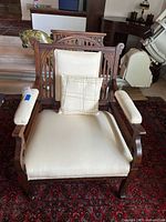 Front view of carved wood armchair with cream upholstery and plaid pillow
