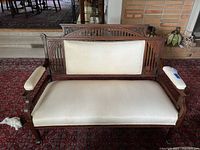 Front view of carved wood settee with cream upholstery