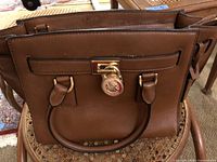 Front view of brown Michael Kors satchel showing padlock and handles