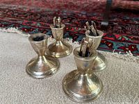 Four weighted sterling silver candle holders grouped on carpet with rug background