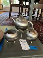 Full view of stainless steel teapot, creamer, sugar bowl with spoon on glass table