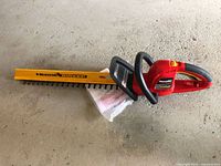 Full view of Homelite hedge trimmer with yellow blade guard and manual