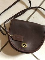 Front view of mahogany leather Coach half-moon bag showing flap and brass turnlock