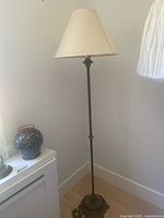 Full view of dark patterned metal floor lamp with smooth angled beige lampshade in a corner.