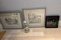 Overall view of two framed art prints and a silver table lamp between them