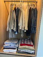 Closet rack with assorted men's pants including denim and light-colored pants, and piles of folded shirts below.
