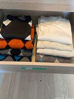 Drawer view with eight folded men's sweaters in assorted colors and argyle patterns