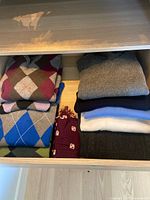 Drawer of neatly folded men's sweaters including argyle patterns and solid colors in various tones