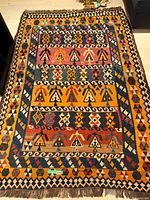 Full view of colourful Persian rug showing geometric patterns in orange, yellow, blue, red, white, and black colors.