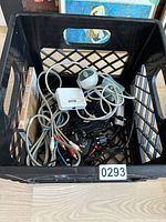 Top-down view of black crate containing assorted cables, chargers, and one Logitech webcam.