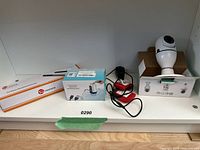Photo showing the cordless scanner, automatic water dispenser box, glove hand warmers, and WiFi panoramic camera box arranged on a shelf.