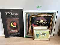 Four assorted framed prints including a black poster for 'Big Bang' alongside colorful abstract prints and an animal illustration, arranged against a white wall.