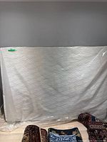 Full view of the Astra full/double mattress wrapped in a clear plastic bag, showing the entire mattress standing upright against a wall.