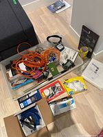 Overall view of assorted gardening and home hardware tools and accessories packed in plastic bins, showing extension cords, tape, tools, and other items.