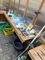 Overview of gardening tools on wooden table including hoses in yellow bin, black pots, gardening hand tools, and outdoor lights