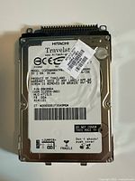 Front view of Hitachi Travelstar hard drive showing label with specifications and barcodes. Shows product model and minor surface wear.
