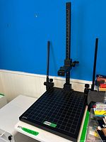 Full view of the Kaiser RS 2 XA copy stand positioned on a table, showing the matte grey baseboard with grid and scale, vertical black anodized column, and the attached adjustable camera arm.