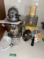 KitchenAid mixer with mixing bowl, whisk and dough hook attachments, and food processor with discs and accessories.