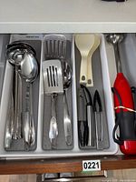 Kitchen utensils including ladles, slotted spatulas, plastic spoons, garlic press, small tongs in tray