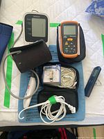 Medical supplies on white quilted surface including Omron blood pressure monitors, CEM thermometer, Life heating pad, DR-HO therapy system, and digital scale.