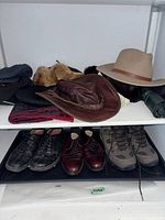 Photo shows three pairs of men's shoes size 9: black casual shoes, burgundy dress shoes, and hiking boots. Above shoes are several hats including a brown leather hat, a beige felt hat, a faux fur hat, and other assorted hats.