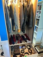 Various men's jackets in denim, fabric, and leather hanging in a wardrobe alongside ties laid on a shelf below.