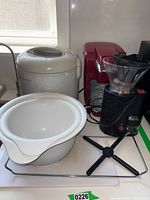 Overview showing rice cooker, coffee machine, coffee grinder, and stacked white plastic bowls on a shelf.