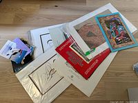 Top view of assorted prints and postcards in plastic sleeves and loose, showing a variety of subjects including an abstract art piece, cultural and nature images, and political/travel postcards.
