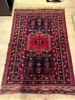 Full view of the rectangular Persian rug showing its red, black, and dark blue geometric patterned design and fringed edges.