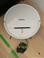 Top side view of white Thinkkitchen Probot robotic vacuum cleaner with charger cable beside it on wooden floor.