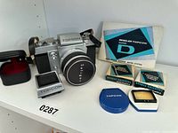 Overview of camera, lens, finder, screens, manual and cases arranged on shelf