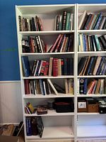 Front view of white bookshelf filled with various books and some small items on lower shelves