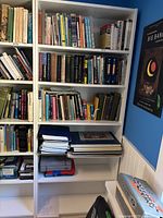 Front view of white bookshelf filled with books and miscellaneous items on shelves, showing six shelves with no damage.
