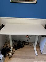 Full frontal view of the desk showing the white tabletop, metal legs, and cable management accessories underneath.