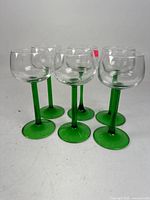 Six crystal glasses standing upright, showing clear bowls and green stems