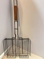 Full view of grill basket standing upright showing handle and basket shape