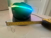 Projector side view with tape measure showing roughly 6.5 in width, LED ring illuminated