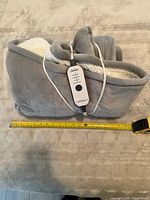 Folded grey electric blanket with controller and tape measure showing size