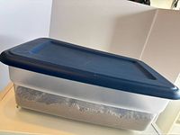 Closed Sterilite bin with blue lid, sand visible inside