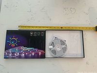 Opened box with reel of LED strip and accessories beside retail sleeve; tape measure for scale
