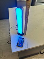 Lamp lit blue standing on countertop with remote and ruler showing height