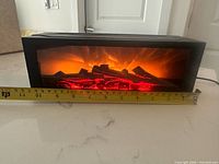 Front view showing faux flame and log effect with tape for width reference