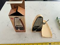 Metronome with lid off showing tempo scale and pendulum alongside original box