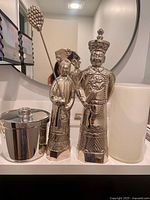 Two silver-tone Asian statues, white glass vase, portion of ice bucket on counter
