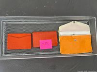 Two orange card holders, silk pouch, and wire mesh basket overall view
